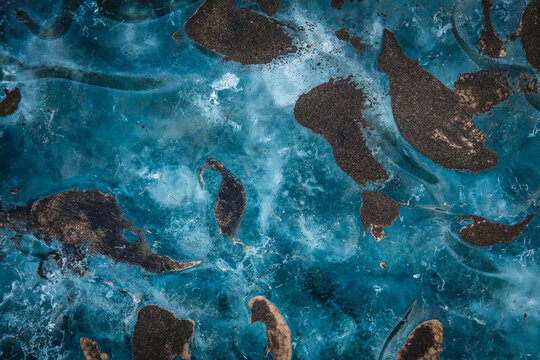 View of the sapphire ice cave's floor, a surreal landscape of frozen turquoise water embracing dark, scattered sediments, creating a mesmerizing contrast, Vatnajokull, Iceland.