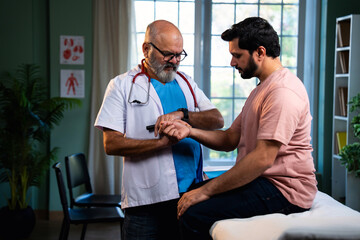 Senior Indian physician uses medical torch to examine young male patient in modern clinic