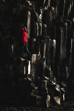 View of a bright red jacket stands out against the dark basalt columns, creating a striking contrast of color and texture at Reynisfjara Beach, Vik, Iceland.