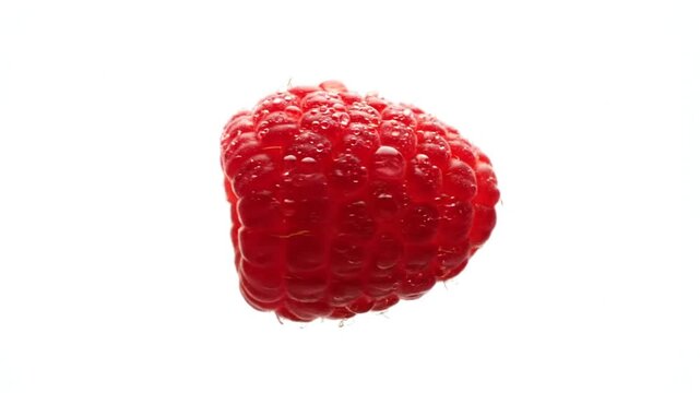 A vibrant raspberry submerged in water, showcasing its rich red color and intricate texture, with bubbles forming around it, set against a stark white background