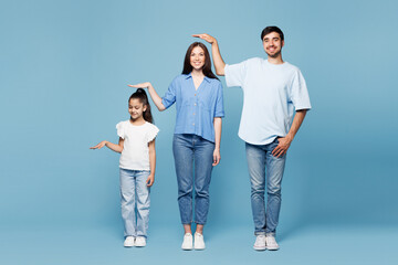 Full body young happy parents mom dad with child kid daughter girl wearing casual clothes put hand above head showing height difference isolated on plain blue background. Family day childhood concept.