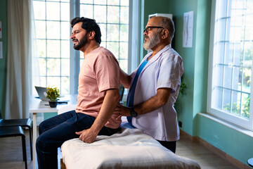 Indian physiotherapist treating back pain of young patient during physical therapy in clinic