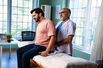 Indian physiotherapist treating back pain of young patient during physical therapy in clinic