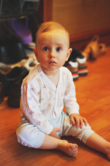 Curious toddler seated on wooden floor by shoes