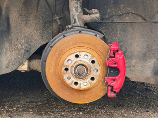 A close-up of a car's exposed brake system, featuring a disc brake with rust evident on the round metal rotor. 
