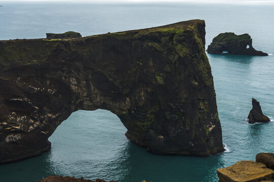 View of rugged, dark cliffs rise majestically from the turquoise sea, sculpted by time and tide into dramatic arches and stacks, Vik, South Island, Iceland.