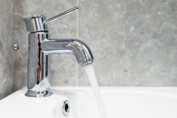 Expensive water flows from a chrome luxury faucet, close-up.