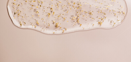 Serum fluid 24k gold gel facial cream flowing on beige pastel background. Beauty cosmetic product smudge, pure transparent lotion with gold particles, skin care jelly serum top view Luxury moisturizer