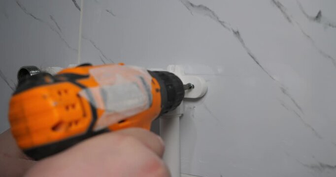 A professional plumber attaches white polypropylene pipes to a bathroom wall. The plumber uses a cordless electric screwdriver to secure the brackets and complete the plumbing system installation.