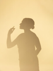 Soft silhouette of a woman clapping hands against a warm beige background, creating a minimalist and artistic shadow composition with calm and emotional atmosphere.