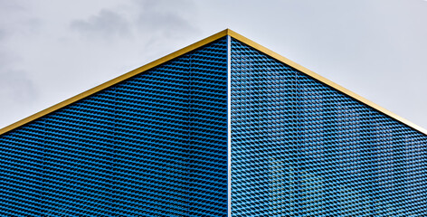 Blue perforated metal mesh wraps a sharp triangular corner with yellow trim, highlighting bold...