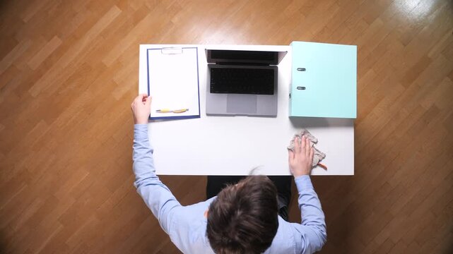 Person disinfecting and wiping down a white office desk with a cloth, maintaining a clean and organized workspace while working from home or in an office environment