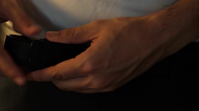 Close-up static shot of hands unlocking and adjusting a leather ratchet belt worn at the waist in an indoor setting