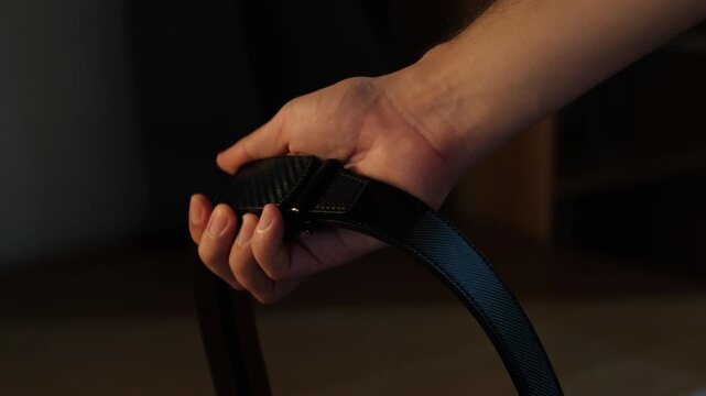 Close-up static shot of a hand holding a leather ratchet belt with buckle in an indoor setting