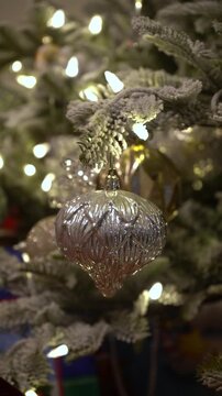 Decorated pine tree with multiple Christmas ornaments surrounded by fake snow, silver reflections, vertical winter backdrop