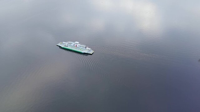 A drone flies above Lake Windermere, trailing slightly left behind the Bowness ferry. One white car is on board as the vessel cuts through calm water, leaving a clear wake on all sides.