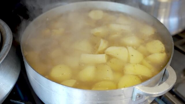 Potatoes are simmering in a metal pot releasing steam as they cook. This culinary process is essential for food preparation and meal planning in the kitchen.