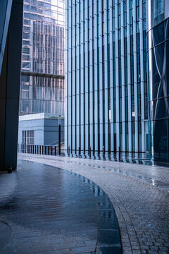 Urban architecture modern alley with curve, cobblestone and glass, wet surfaces, empty perspective and moody leading lines, quiet downtown