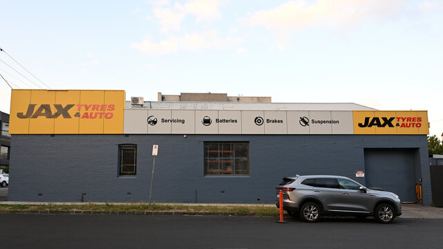 Side of Jax Tyre and Auto service centre building, featuring large yellow signs with company logo, late in the day