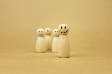 Happy wooden peg doll standing out from the crowd with diverse emotions. Leadership, positive attitude, and customer satisfaction concept represented by wood figures on brown background.