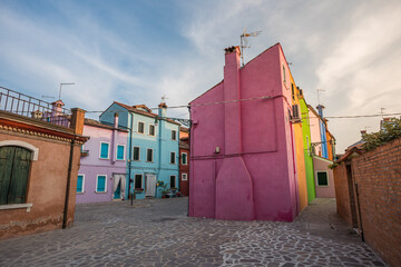 Colorful houses of Burano island near Venice showcasing vibrant pastel facades, narrow streets, and traditional Italian architecture in a quiet residential square under soft daylight sky