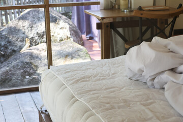 Cozy interior of safari lodge bedroom with untidy white bed linen next to glass window overlooking rocky nature landscape with wild animal resting calmly outside © CoreRock