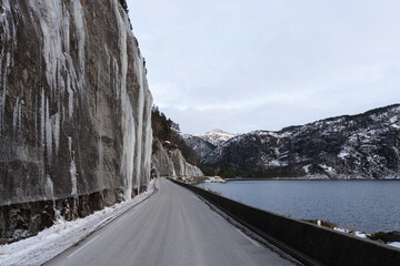 Narrow winter road along fjord with icy cliff and rockfall protection in Norway