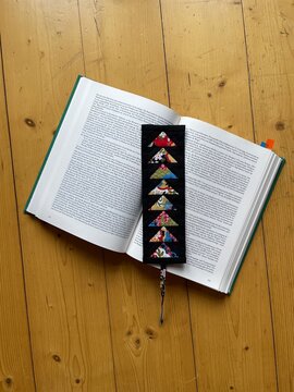 Handmade fabric bookmark featuring intricate foundation paper piecing (FPP) Flying Geese pattern, crafted from colorful patchwork triangles in Japanese, floral, and geometric prints.