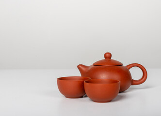 ceramic teapot with two small bowl cups arranged on table. Warm terracotta color and rounded forms