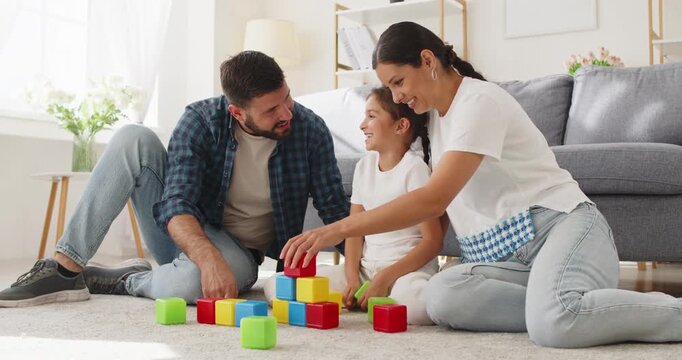 Family parents and daughter play toys home. They sit on the livingroom carpet arranging blocks and cubes, guiding learning, patience, and cooperation. Playful learning and family bonding.