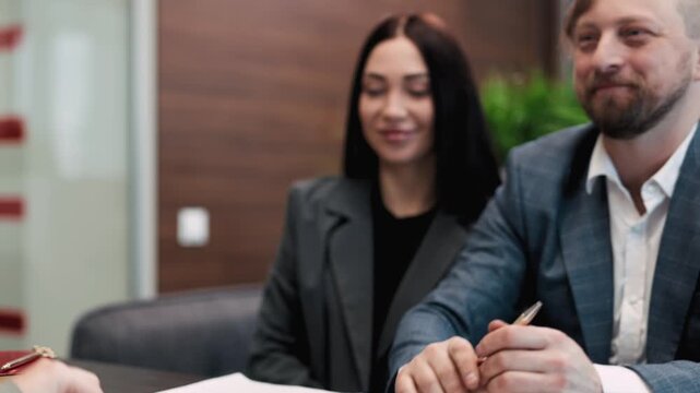 Business professionals engaged in a transaction, exchanging documents and signing agreements, showcasing the process of negotiation and finalizing a sale in a modern office setting