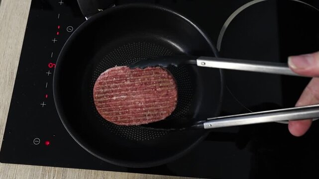 Cuisson d'un steak hach&eacute; dans une po&ecirc;le sur une plaque de cuisson en c&eacute;ramique.