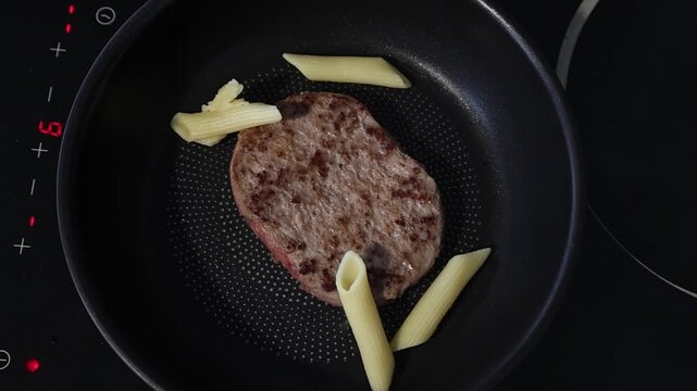 Cuisson d'un steak hach&eacute; dans une po&ecirc;le sur une plaque de cuisson en c&eacute;ramique.