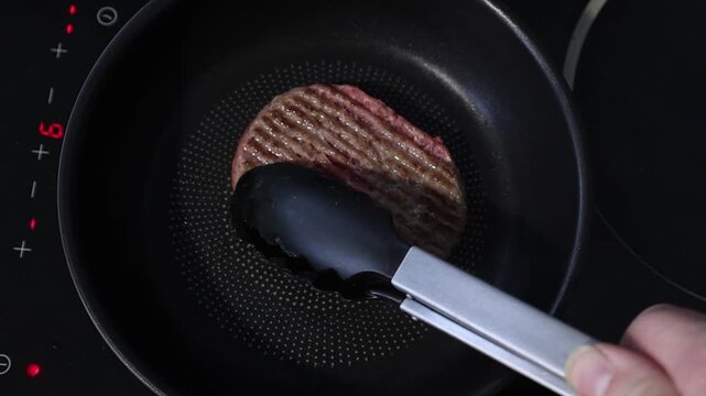 Cuisson d'un steak hach&eacute; dans une po&ecirc;le sur une plaque de cuisson en c&eacute;ramique.