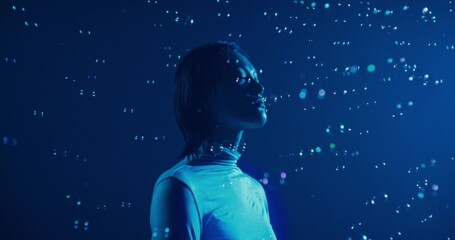 Portrait of a serious, focused woman among soap bubbles. She stands in the blue studio light.