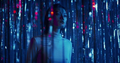 A serious young woman stands among the sparkling blue tinsel. She touches the tinsel with her hands