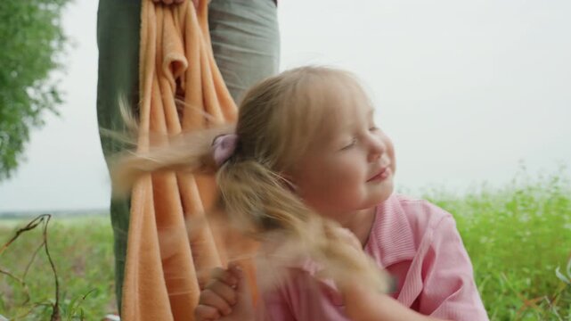 caucasian child exploring towel near birch trees in meadow, closeup of ponytailed preschooler inspecting fabric, ribbon bows, pensive smiles, collecting wildflowers, gentle breeze, candid portrait