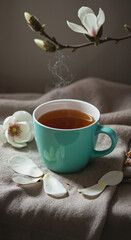 Hot tea in turquoise cup with magnolia flowers on linen background  