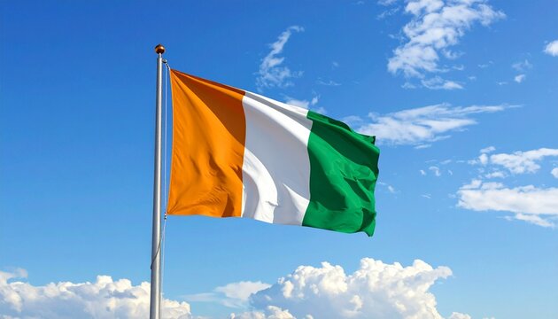 Ivory Coast flag waving on flagpole against bright blue sky with clouds, national tricolor symbol