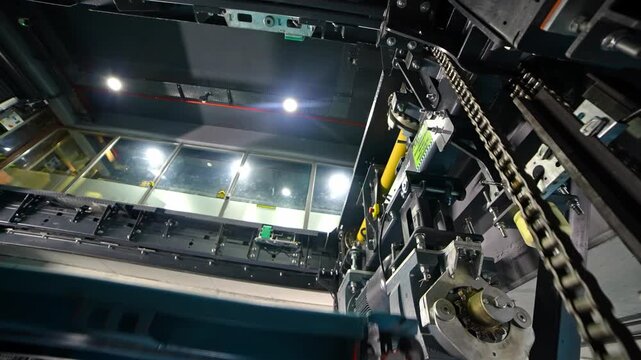 A detailed close-up view of a chain-driven lift mechanism inside an automated robotic parking system, showing metal structures, moving components, and a vehicle positioned on the platform.