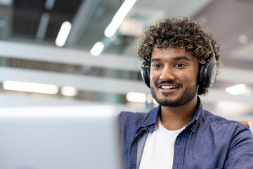 Close-up photo of a young Indian man wearing headphones working and studying with a laptop