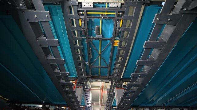 A clean view of the central rail corridor inside an automated robotic parking system, featuring steel columns, lighting, blue platforms, industrial pipes, and the main shuttle track in a high-tech fac