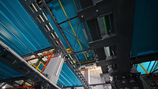 A clean view of the central rail corridor inside an automated robotic parking system, featuring steel columns, lighting, blue platforms, industrial pipes, and the main shuttle track in a high-tech fac