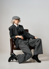 Stylish woman in vintage suit and flat cap posing in a chair