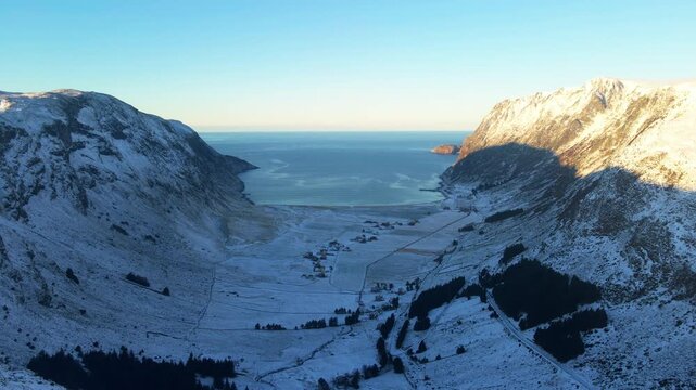 Scenic drone shot over Hoddevik, a famous surfing place at the west coast in Norway looking out to the horizon with snow covering the landscape and the sun shining on the mountains and