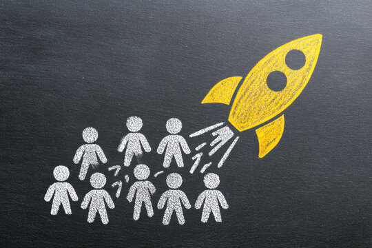 Conceptual illustration of a yellow rocket launching from a group of white chalk-drawn people symbolizing innovation and leadership on a blackboard background