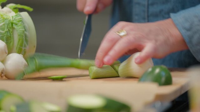 Detail of a chef's hand slicing green onions and leeks for a meal