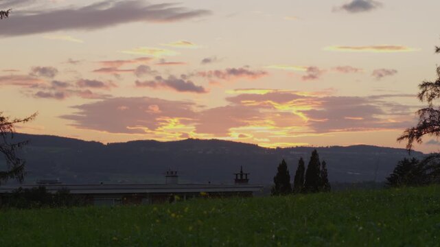 Sunset view of a hill with forest from a green field in late summer, Switzerland