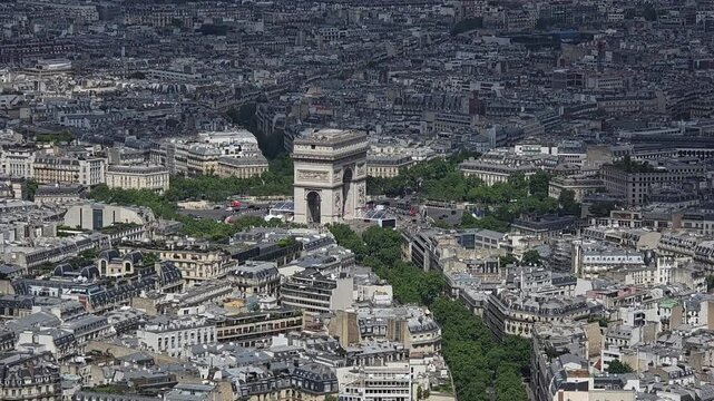 Aerial drone view of Paris showing Arc de Triomphe surrounded by dense city buildings, tree lined avenues, and classic urban layout. Iconic French capital scene for travel and tourism