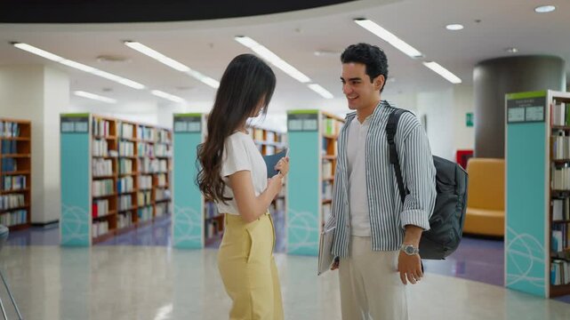 Two multi-ethnic university students standing and greeting each other while chatting in a university library, exchange student program concept